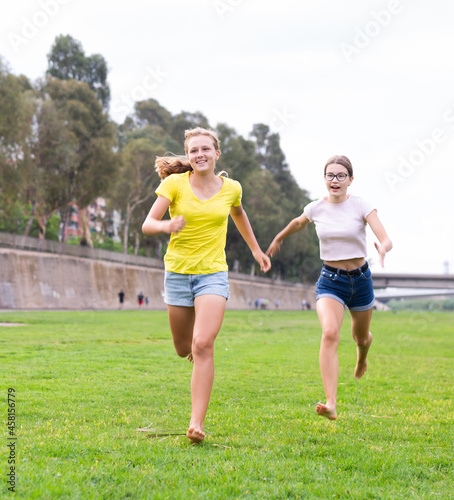 Fototapeta Naklejka Na Ścianę i Meble -  Two young barefoot girls in shorts running on meadow together.