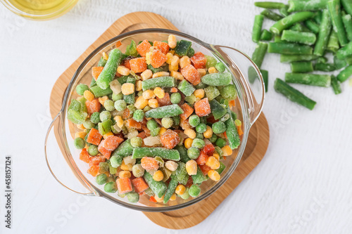 Bowl with different frozen vegetables on light background