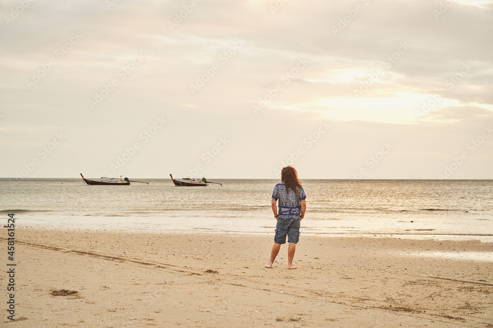 Unrecognizable person standing on an empty beach with two long tail boats