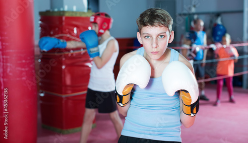 Portrait of young serious teenager with boxing gloves posing at gym..