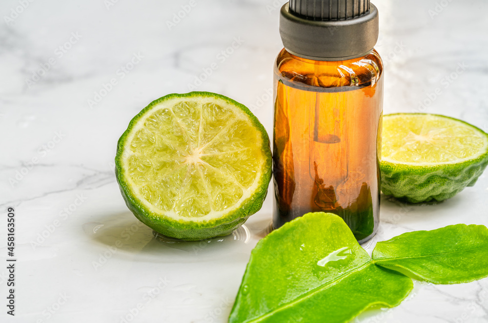 Beautiful packshot of Bergamot essential oil in a small brown glass bottle with fresh bergamot fruit with green leaf on the marble tabletop, wet of water. Blank space on the bottle for branding. - obrazy, fototapety, plakaty 