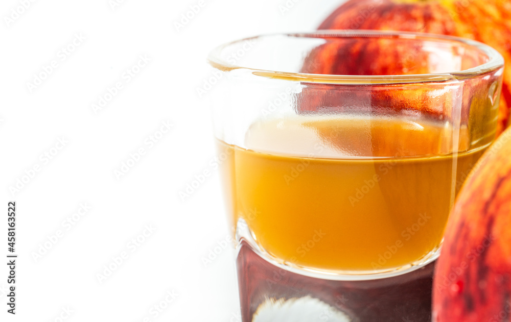 Close up organic Apple Cider Vinegar with the mother in a small glass shot, two red apples is aside of the glass, image on white background. Blank space for text. Close up organic Apple Cider Vinegar with the mother in a small glass shot, two red apples is aside of the glass, image on white background. Blank space for text.