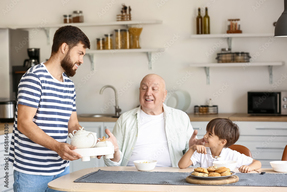 Obraz premium Happy man, his little son and father having breakfast in kitchen