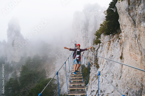 A young man in mountaineering equipment walks uphill on a suspension bridge in the fog.  Heavenly trail. Suspension bridge on Mount Ai-Petri, Yalta, Crimea. Sea coast in Crimea. 