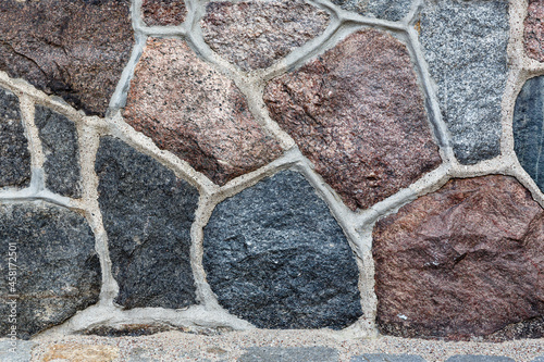 Fragment of old masonry with a concrete seam, made of stones of different colors.