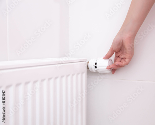 A woman's hand holds the heating thermostat handle. Heating service cost concept, utility price increase. Copy space for text