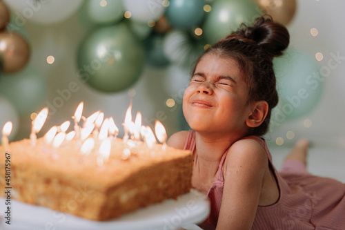 Φωτογραφία Little dark-skinned girl makes a wish and blows out the candles on the birthday cake