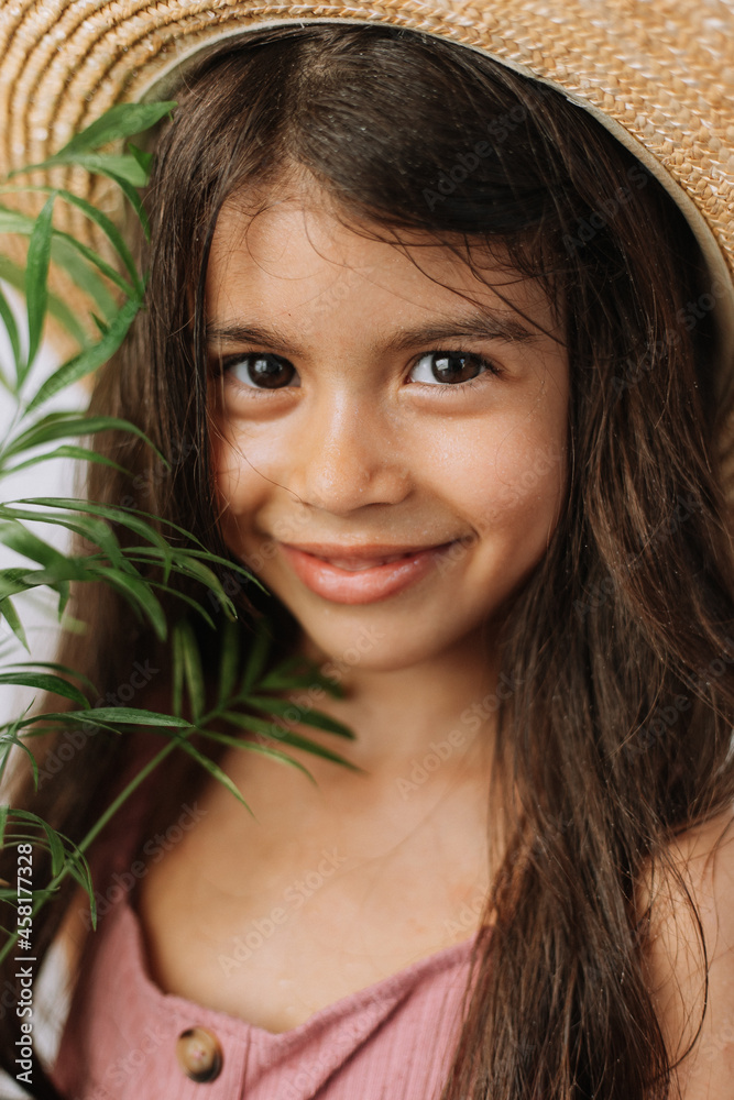 Face of a little girl surrounded by tropical leaves. Closeup portrait of a beautiful swarthy baby with perfect skin and dark hair. Natural cosmetics, health, cleanliness, skin care, beauty concept Face of a little girl surrounded by tropical leaves. Closeup portrait of a beautiful swarthy baby with perfect skin and dark hair. Natural cosmetics, health, cleanliness, skin care, beauty concept