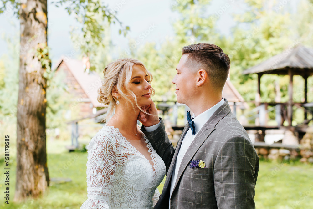 Portrait of beautiful young married couple outdoors, happy groom caresses, flirts with bride with closed eyes, strokes her face with his hand. Wedding day, just married, love and romance concept Portrait of beautiful young married couple outdoors, happy groom caresses, flirts with bride with closed eyes, strokes her face with his hand. Wedding day, just married, love and romance concept