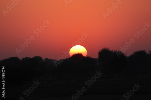 full round yellow bright sun and dim sunlight,Sunset behind silhouette wild trees and small hill, The full brightness and sharp of the sun in the open pure atmosphere and in the countryside