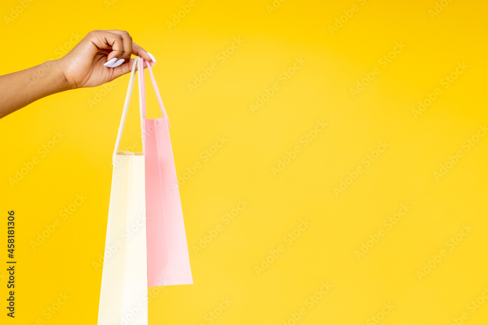 Purchase delivery. Online shopping. Retail promotion. Closeup of black woman hand holding bags isolated on orange empty space background.