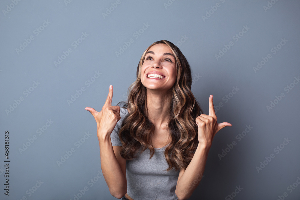 Portrait of an excited joyful woman pointing finger up over gray background.