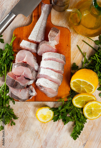 Ingredients for cooking. Raw merling fish steaks on wooden table with fresh parsley and sliced lemon photo