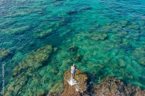 Fisherman throwing a fishing line while standing on a shallow lagoon rock  Aerial view.