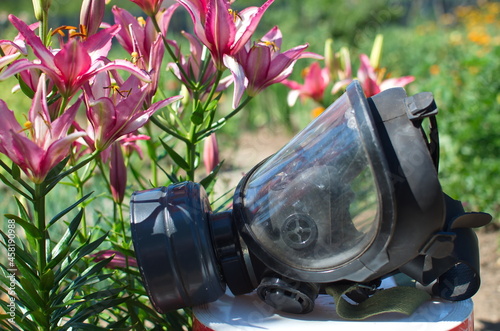 Environmental protection, gas mask lying next to flowers on the background of a green meadow