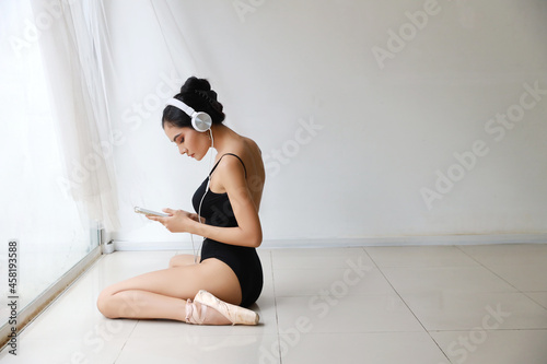 Stunning shape of charming asian woman wearing black sportswear sitting with headphone. Beautiful girl listening music from mobile phone while training ballet dancing (technology and healthy concept)