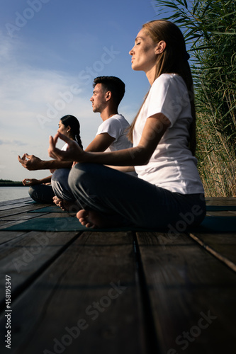 Group of people doing yoga exercises by the lake at sunset.