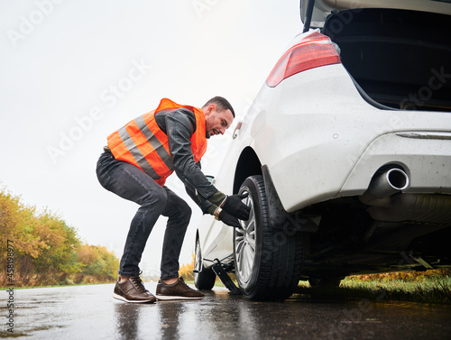 Foto Roadside assistance worker removing flat tire while repairing car on the street