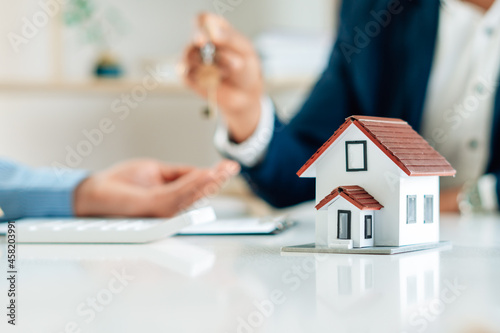 Real Estate Broker Or businessman holding white house model and house key in hand.Mortgage loan approval home loan and insurance concept.