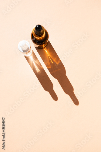 Glass bottles of cosmetic liquids, arranged in a row on the pastel beige surface, cast shadows. Flat style, copy space. Vertical image. photo