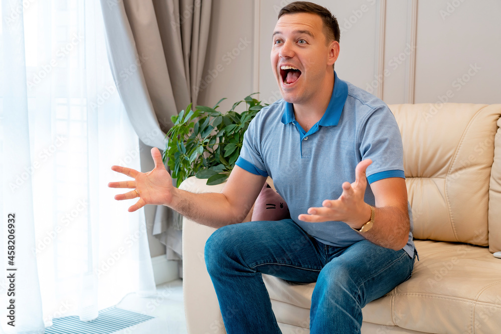 Man watching football in living room. Millenial man at home alone watching soccer games on tv enjoying and celebrating goal and gestures of victory sitting on couch happy and excited Man watching football in living room. Millenial man at home alone watching soccer games on tv enjoying and celebrating goal and gestures of victory sitting on couch happy and excited
