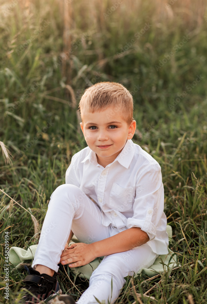 A small handsome boy blonde in a white shirt and white pants in nature in the summer. Happy childhood. Positive emotions A small handsome boy blonde in a white shirt and white pants in nature in the summer. Happy childhood. Positive emotions