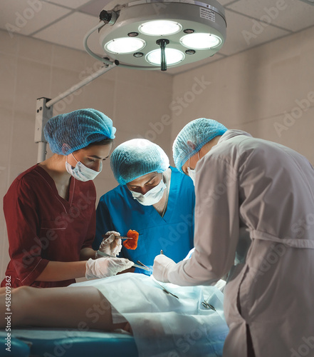 Fototapeta Naklejka Na Ścianę i Meble -  Group of surgeons at work operating in surgical theatre. Resuscitation medicine team wearing protective masks holding steel medical tools saving patient. Surgery and emergency concept.