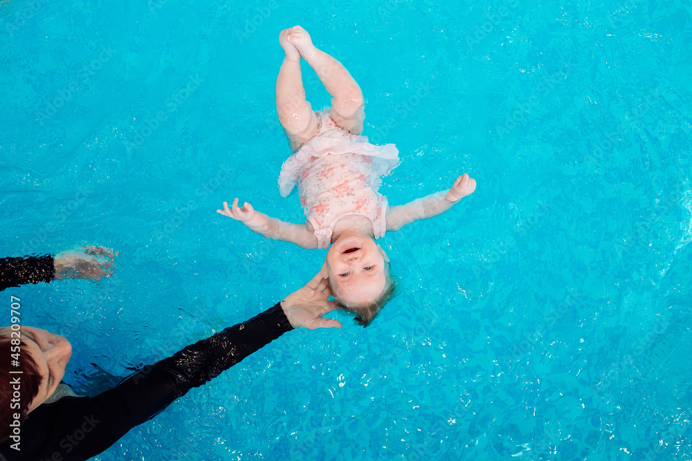 A swimming teacher teaches a kid to swim in the pool.