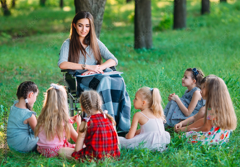 Disabled teacher conducts a lesson with children in nature. Interaction of a teacher in a wheelchair with students.