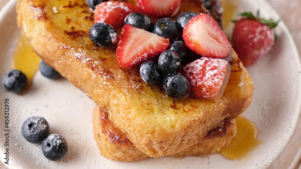 Eating French toast with berries and syrup. Cutting sweet french toast with fork and knife Eating French toast with berries and syrup. Cutting sweet french toast with fork and knife