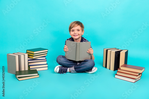 Full length photo of nice little boy read book wear t-shirt jeans sneakers isolated on teal background