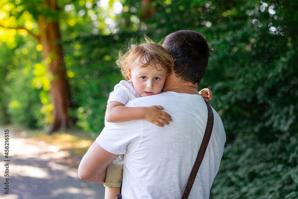 Father carries his tired little son after a long walk in a park in summer. Sleepy exhaused toddler boy resting in daddy's arms. Father carries his tired little son after a long walk in a park in summer. Sleepy exhaused toddler boy resting in daddy's arms.
