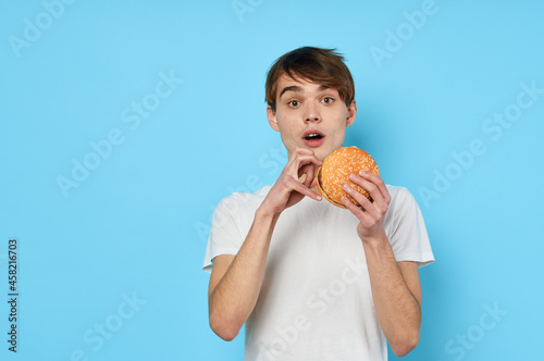 a man in a white t-shirt with a hamburger in his hands lunch blue background