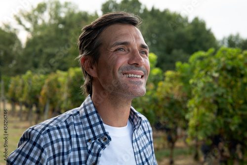 Close up of happy successful farmer or winemaker is smiling satisfied in the middle of vine branches rows during wine harvest season in vineyard for further high quality wine production