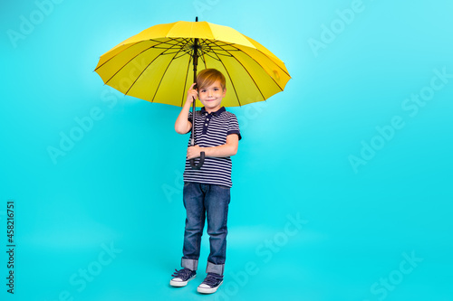 Full body photo of optimistic little boy hold umbrella wear t-shirt jeans sneakers isolated on teal background