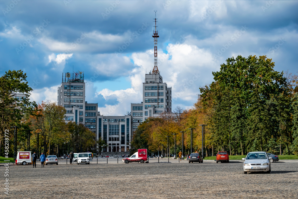 Kharkiv, Ukraine - October 20, 2020: View of Derzhprom building among yellow autumn trees on Svobody Square in Kharkiv. Urban landscape with Soviet skyscrapers on the backdrop of a dramatic cloudy sky