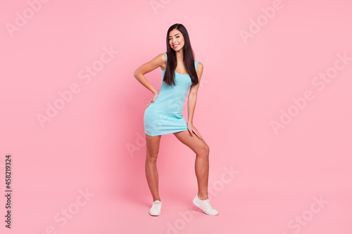 Full length photo of pleasant brunette hairdo young lady stand wear blue dress sneakers isolated on pink color background