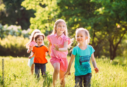 Large group of kids, friends boys and girls running in the park on sunny summer day in casual clothes .