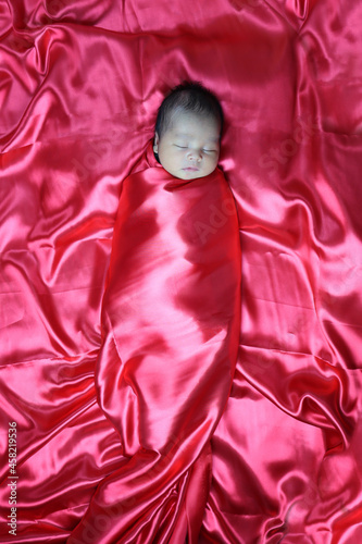 Asian baby boy sleeping comfortably in red cloth.