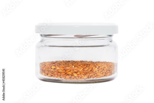 Flax seeds in a transparent glass jar with a lid. Isolated on white background. Condiments and spices.