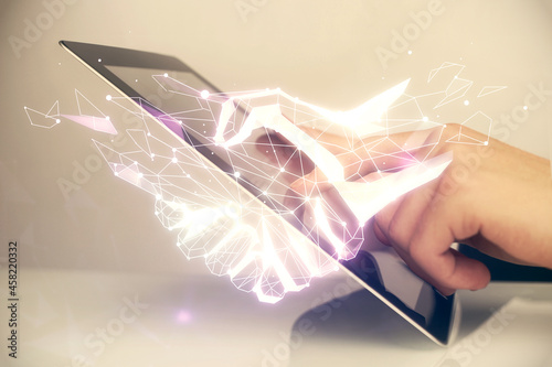 Double exposure of man's hands holding and using a digital device and handshake drawing. Partnership concept.