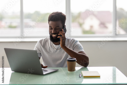 African black man talking on mobile cell phone to clients in office with laptop computer