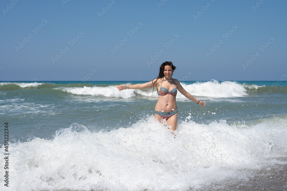 Young woman in a white shirt is bathes in the waves in the sea foam on an exotic tropical island