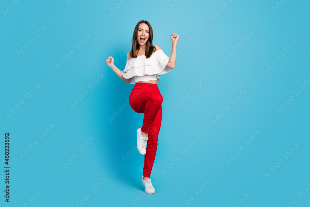 Photo of impressed lucky young woman dressed white blouse smiling rising fists isolated blue color background