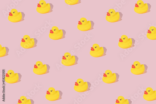 Creative pattern made with yellow rubber duck on pastel pink background. Surreal bathing concept. Retro style aesthetic idea.
