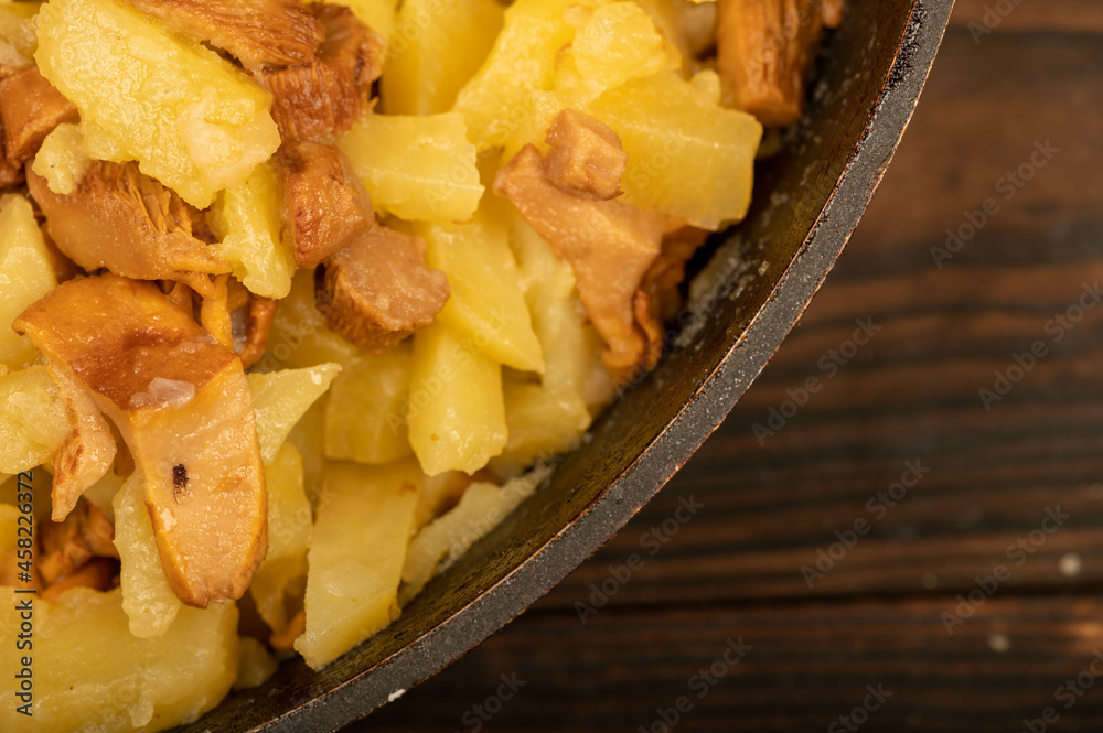 Potatoes fried in a frying pan with mushrooms on a wooden table. A traditional village dish. Potatoes fried in a frying pan with mushrooms on a wooden table. A traditional village dish.