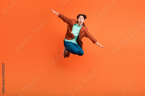 Full size photo of smiling guy jumping fooling around hands wings plane fly isolated on orange color background