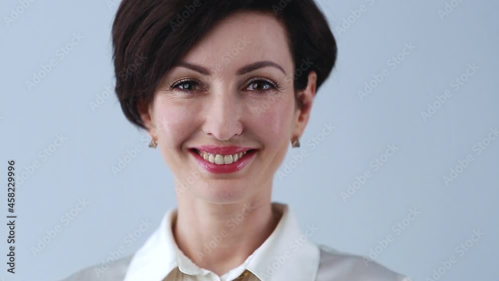 Video portrait of happy business woman with red lipstick, bob haircut wearing formal silk shirt in studio. Beautiful female model in 40s posing with friendly toothy smile Video portrait of happy business woman with red lipstick, bob haircut wearing formal silk shirt in studio. Beautiful female model in 40s posing with friendly toothy smile