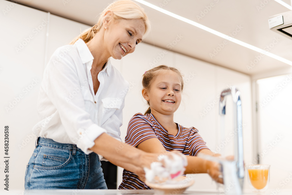White mother and daughter smiling while washing dishes together White mother and daughter smiling while washing dishes together