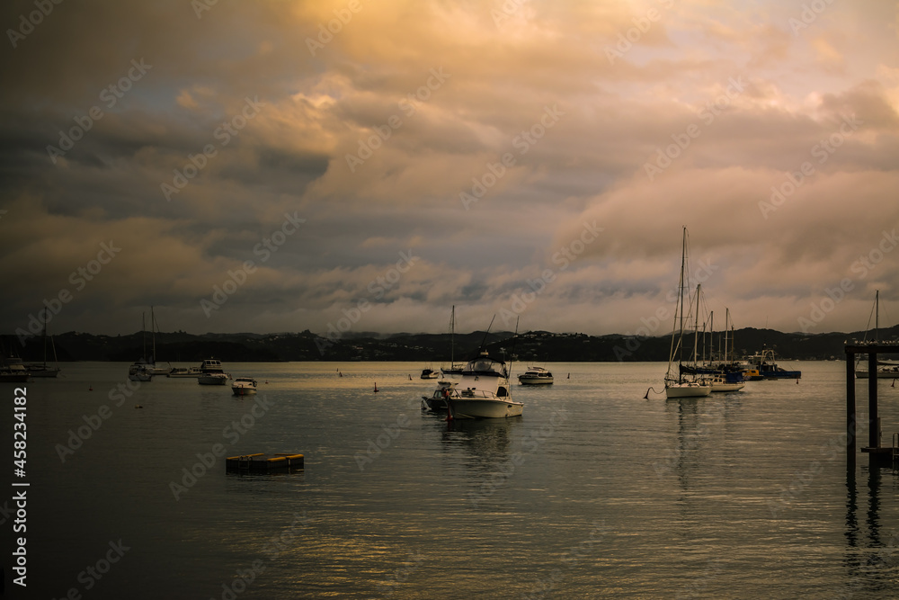 Sunset colours reflected in calm waters of a small harbour. Fishing and sailing boats anchored near the coastrline.